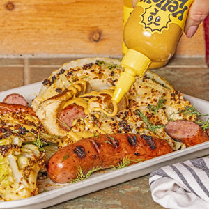Garlic Shiitake hot sauce being squeezed onto a plate with bratwurst and cooked cabbage. 